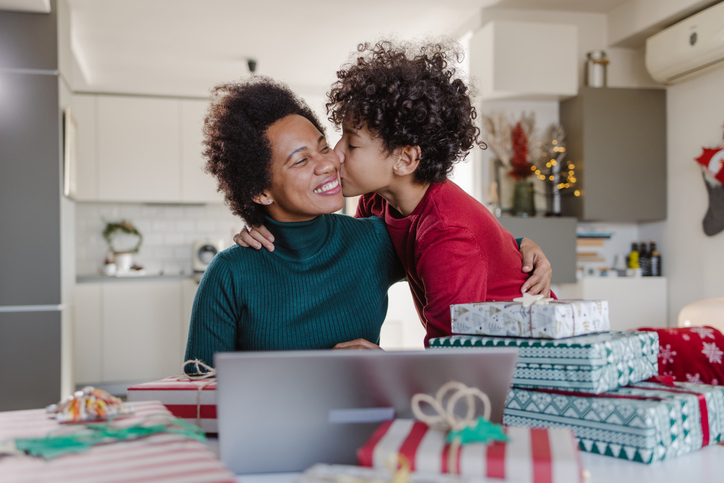 An African American woman getting a warm kiss on the cheek by her young mixed race son, while doing some online Christmas shopping