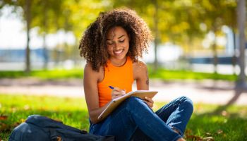 Portrait young woman sitting on grass writing in book