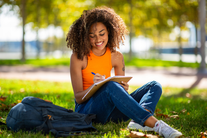 uplift your spirits - Portrait young woman sitting on grass writing in book