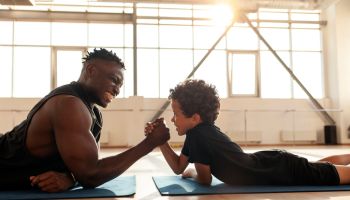 African American man with his son is engaged in arm wrestling in the gym, dad measures his strength with his son
