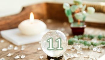 Number eleven on Gemstone sphere or crystal balls known as crystallum orbis and orbuculum. Natural clear quartz ball on stand on wood tray in home. Predictions concept.