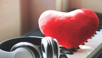 red heart shape pillow with headphones on piano keyboard. Love song or valentine's day concept.