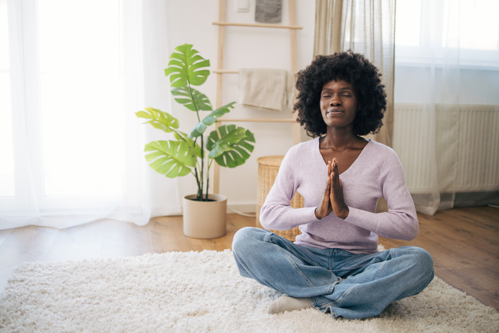 Young woman meditating with hands in prayer at home.