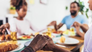 A multi-generational African-American family saying grace at dinner table and holding hands