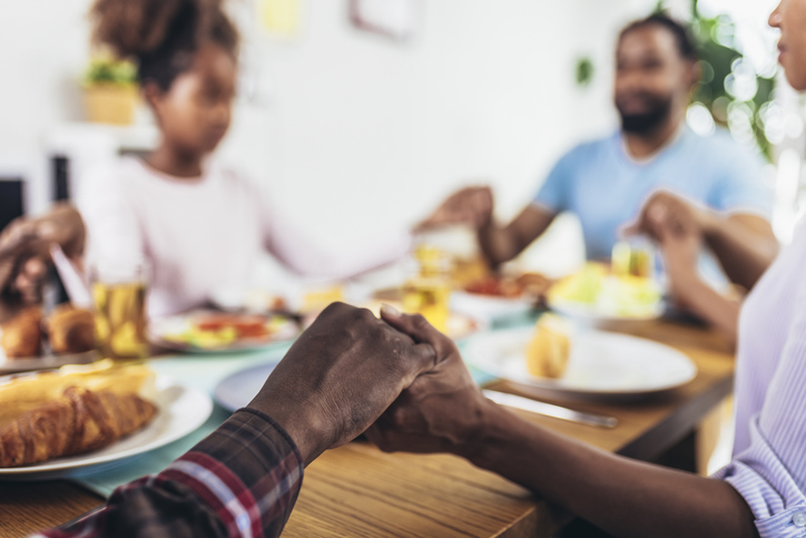 A multi-generational African-American family saying grace at dinner table and holding hands