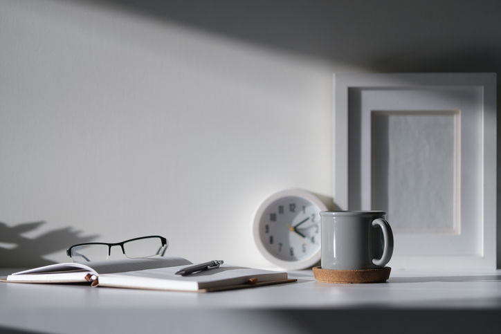 Creative workspace with blank poster frame, camera, coffee cup and houseplant on wood table.