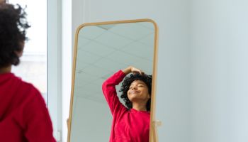 Love yourself. Beautiful young smiling african american woman dancing touching curly hair enjoying her mirror reflection. Black lady looking at mirror looking confident and happy. Self love concept.