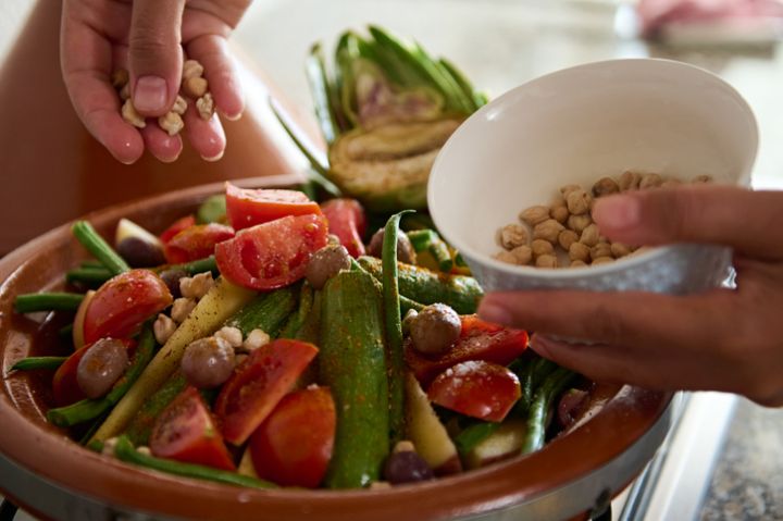 Closeup of the hands of a housewife adding chickpeas into a meal while cooking healthy vegetarian meal in tagine