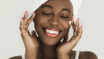 Smiling african american applying face cream on her perfect skin.