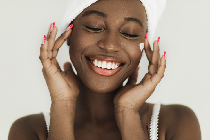 Smiling african american applying face cream on her perfect skin.