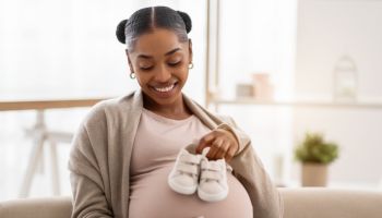 Joyful beautiful pregnant african american woman holding baby booties