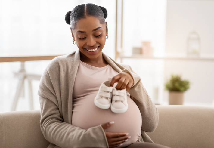 Joyful beautiful pregnant african american woman holding baby booties