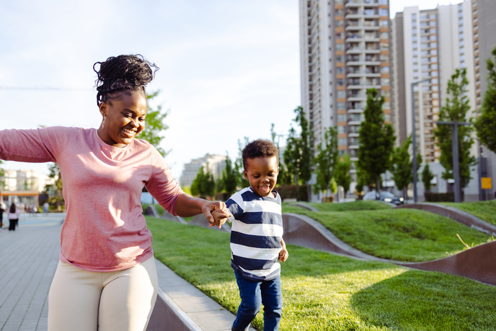 A young African American woman is holding her young son's hand, while he's walking on the side of the road