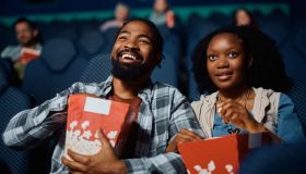 Happy black couple eating popcorn while watching movie in theater.