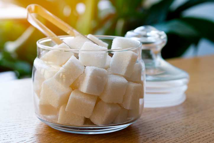 Lump sugar in a transparent glass sugar bowl, on a wooden table or background, at home, in a cafe, cafeteria or restaurant. The concept of poor nutrition and lifestyle.