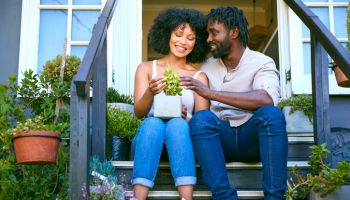 Couple Sitting On Steps Outside At Home Looking After Garden Plants