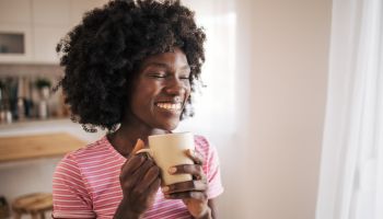 Happy African American woman drinking a cup of coffee at home and smiling
