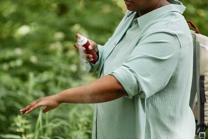 Side view closeup of black woman spraying arms with bug repellent outdoors