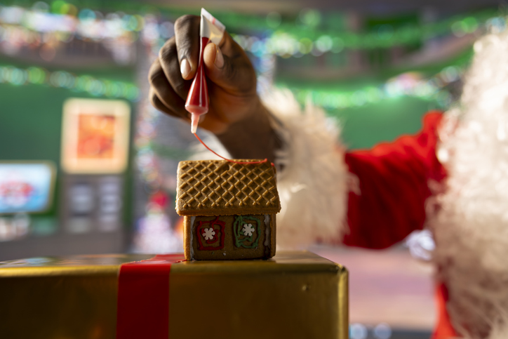 Santa Claus adds icing on homemade cookies to create a gingerbread house