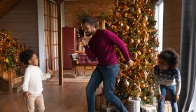 Happy biracial father and kids dance near fir tree