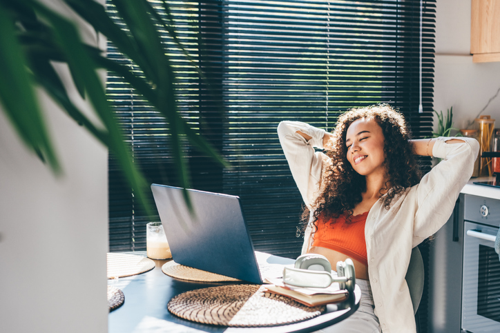 Young woman with laptop relaxes while working in the kitchen.
