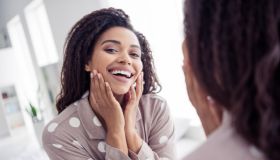 Beautiful woman wearing polka dot pajama smiling joyfully in the mirror at home in the morning, showcasing natural beauty and happiness