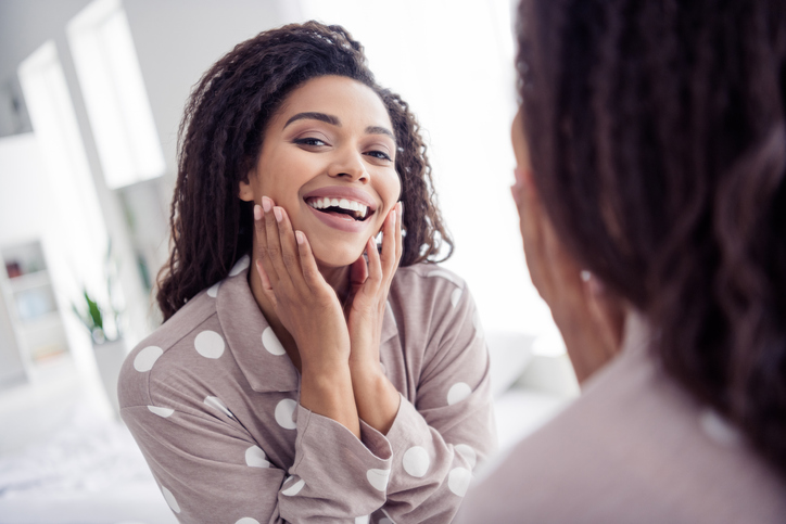 Beautiful woman wearing polka dot pajama smiling joyfully in the mirror at home in the morning, showcasing natural beauty and happiness