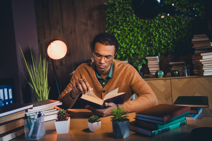 Books Every African American Should Read - Young student studying at home with books and plants, focused on learning, indoors in the evening under warm natural light.