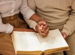 Bible, holding hands and reading with a black couple together in the home for religion, faith or belief in God. Jesus, pray or book with a christian man and woman learning about the spiritual christ