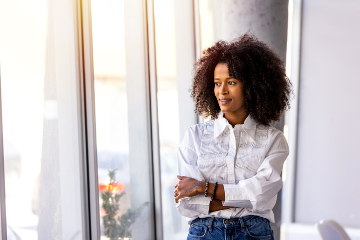 Confident Woman Looking Out of Window in Bright Modern Workspace